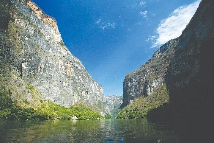 Calm waters reflecting the massive cliff faces in Sumidero Canyon under blue sky