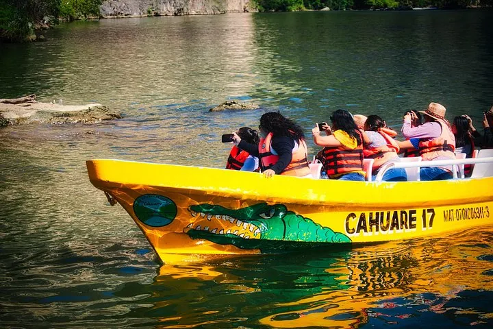 Tourists taking photos from a bright yellow boat adorned with a painted crocodile